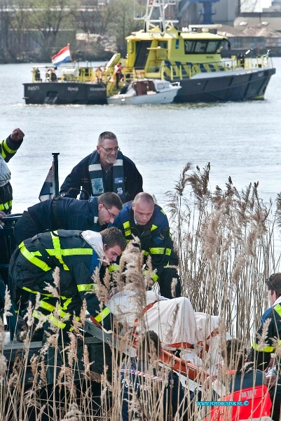 10040808.jpg - FOTOOPDRACHT:Papendrecht:08-04-2010:Foto: 1 van de drenkelingen word aan wal gebracht op de achtergrond het overvaren speedbootje.AANVARING TUSSEN BINNENVAARTSCHIP EN TANKER PAPENDRECHT  Bij een aanvaring tussen een lege binnenvaarttanker en een pleziervaartuig op 8 april rond 14.15 uur op de rivier de Beneden Merwede bij Papendrecht zijn twee opvarenden van het pleziervaartuig te water geraakt. Het gaat om een 60-jarige man uit Dordrecht en een 26-jarige plaatsgenote. Beiden zijn met onderkoelingsverschijnselen voor controle naar een ziekenhuis overgebracht. Hoe de aanvaring heeft kunnen plaatsvinden is nog niet geheel duidelijk. Het onderzoek ligt in handen van de Waterpolitie, onderdeel van het Korps Landelijke Politiediensten. Wel is duidelijk dat twee opvarenden te water raakten. Mensen van een ander binnenvaartschip en personeel van Rijkswaterstaat konden hen net op tijd uit het water halen en naar de kant brengen. Daar stonden meerdere ambulances en een traumahelikopter klaar voor de medische hulp. De toestand van de slachtoffers lijkt mee te vallen. Doordat in de eerste minuten van het incident nog niet duidelijk was hoeveel mensen te water waren geraakt, is opgeschaald tot Grip 1 en waren de hulpdiensten in groten getale aanwezig. Al snel was duidelijk dat het aantal mensen dat in het water terecht was gekomen tot twee beperkt was gebleven en dat er niemand vermist was. Het pleziervaartuig raakte zwaar beschadigd en is door Rijkswaterstaat aangehaakt en naar de kant gebracht. De tanker bleef nagenoeg onbeschadigd en kon op eigen kracht naar de dichtstbijzijnde kade varen. Het scheepvaartverkeer werd niet gestremd Deze digitale foto blijft eigendom van FOTOPERSBURO BUSINK. Wij hanteren de voorwaarden van het N.V.F. en N.V.J. Gebruik van deze foto impliceert dat u bekend bent en akkoord gaat met deze voorwaarden bij publicatie. EB/ETIENNE BUSINK